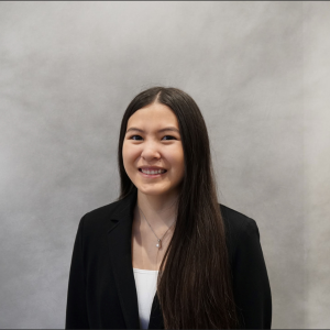 Taylor Morika in a black blazer and white blouse smiling at the camera in front of a gradient gray professional backdrop